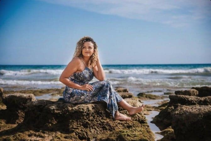 Daiane Tomaz, fotógrafa lifestyle em Albufeira, no Algarve, sentada nas rochas à beira-mar.